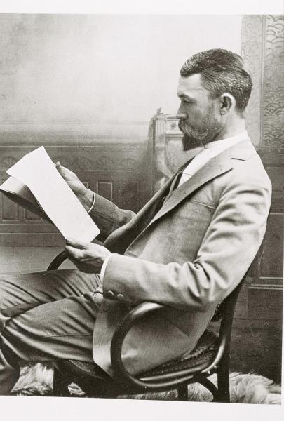 Black and white photo of Adam Clark Vroman reading in a chair